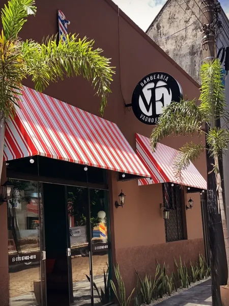 Fachada real da Barbearia Vagno França, com toldo listrado e a placa VF.